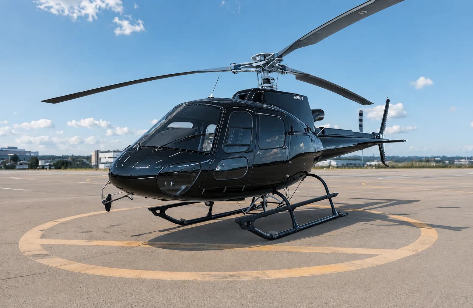A sleek black Airbus H125 helicopter is parked on a helipad under a bright blue sky.