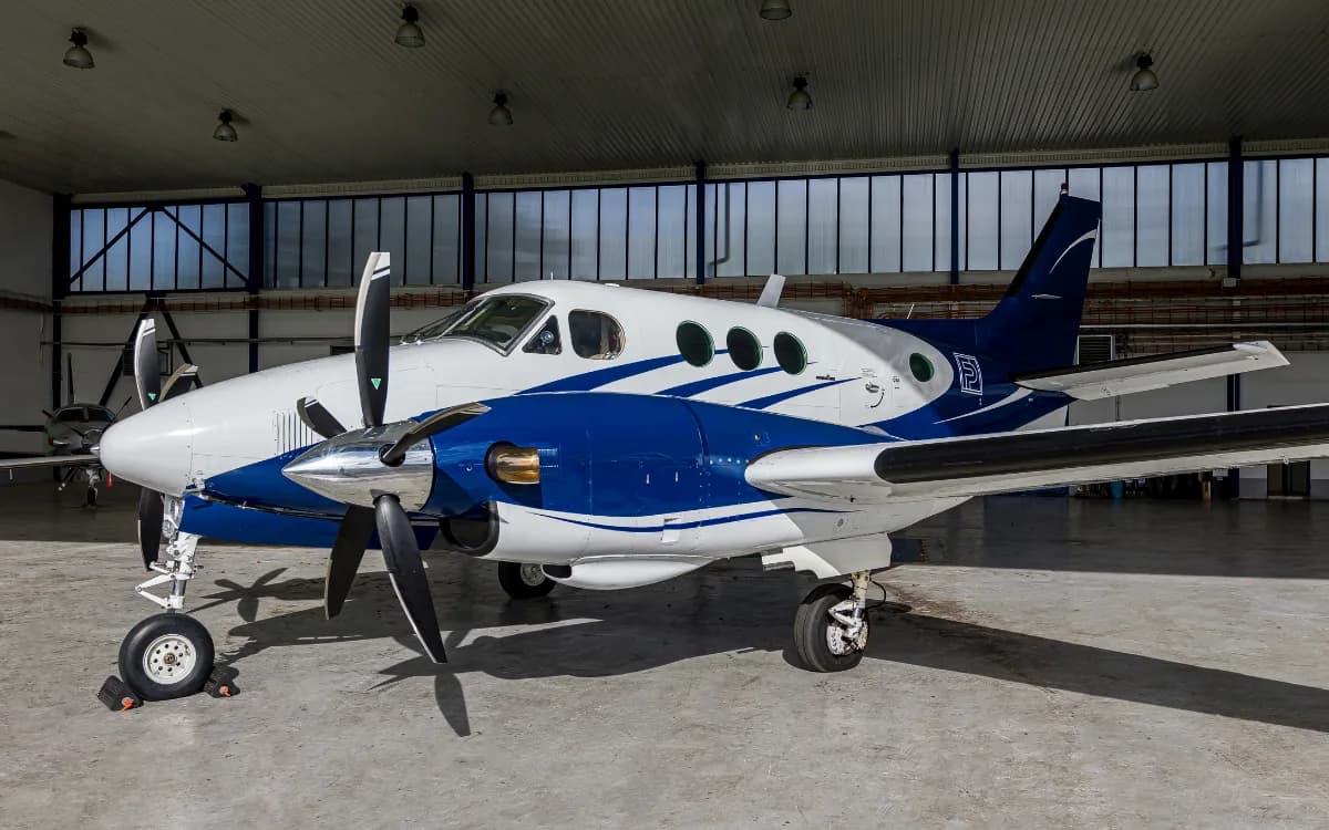 A white and blue Beechcraft King Air C90 twin-turboprop aircraft parked inside a hangar.