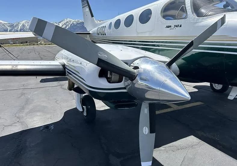 A close-up view of the right engine and propeller of a white and dark green Cessna 340A (N340GC) on an airport tarmac.