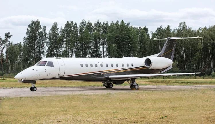 An Embraer Legacy business jet parked on a grassy airfield.