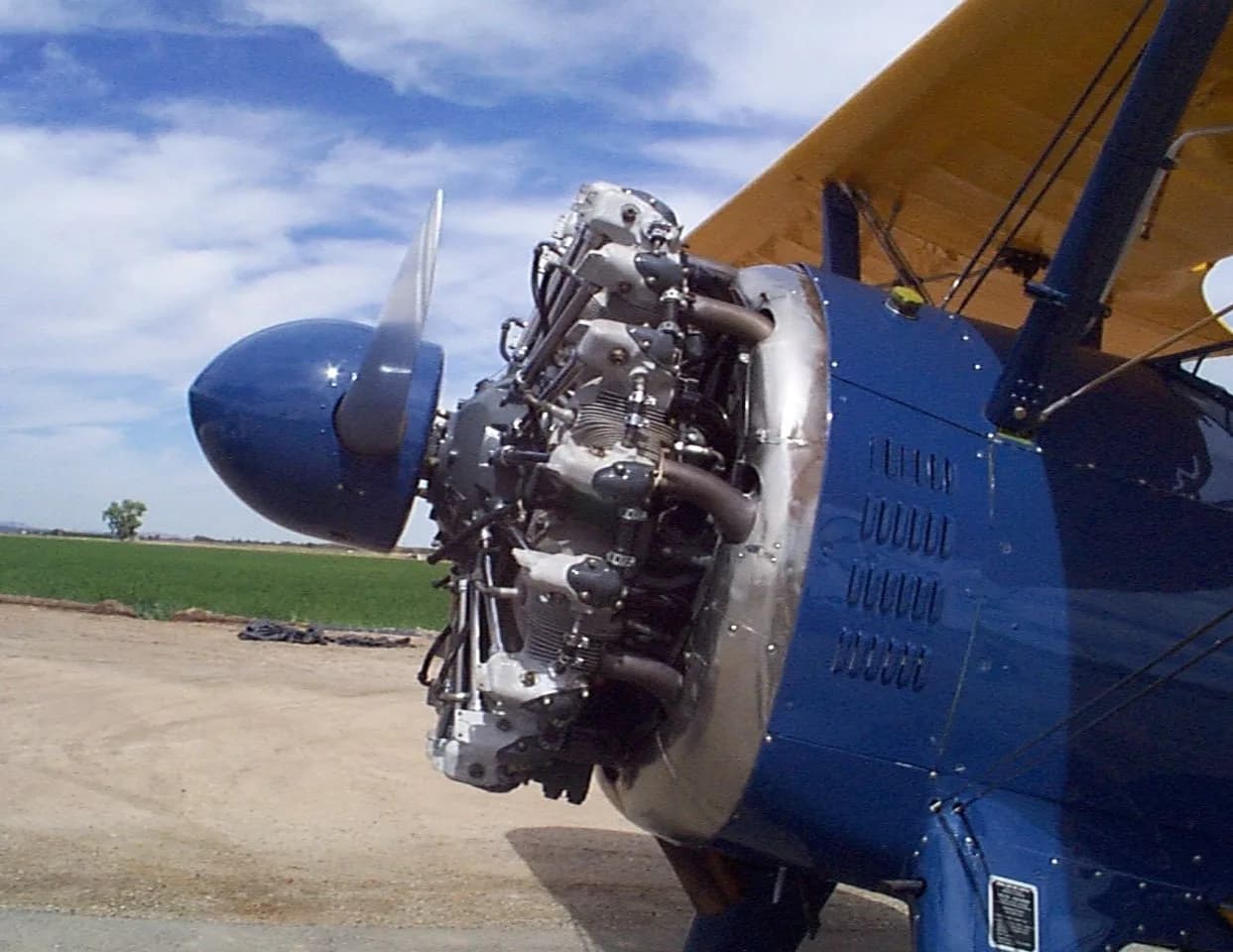 A close-up view of the radial engine and propeller of a blue and yellow biplane.