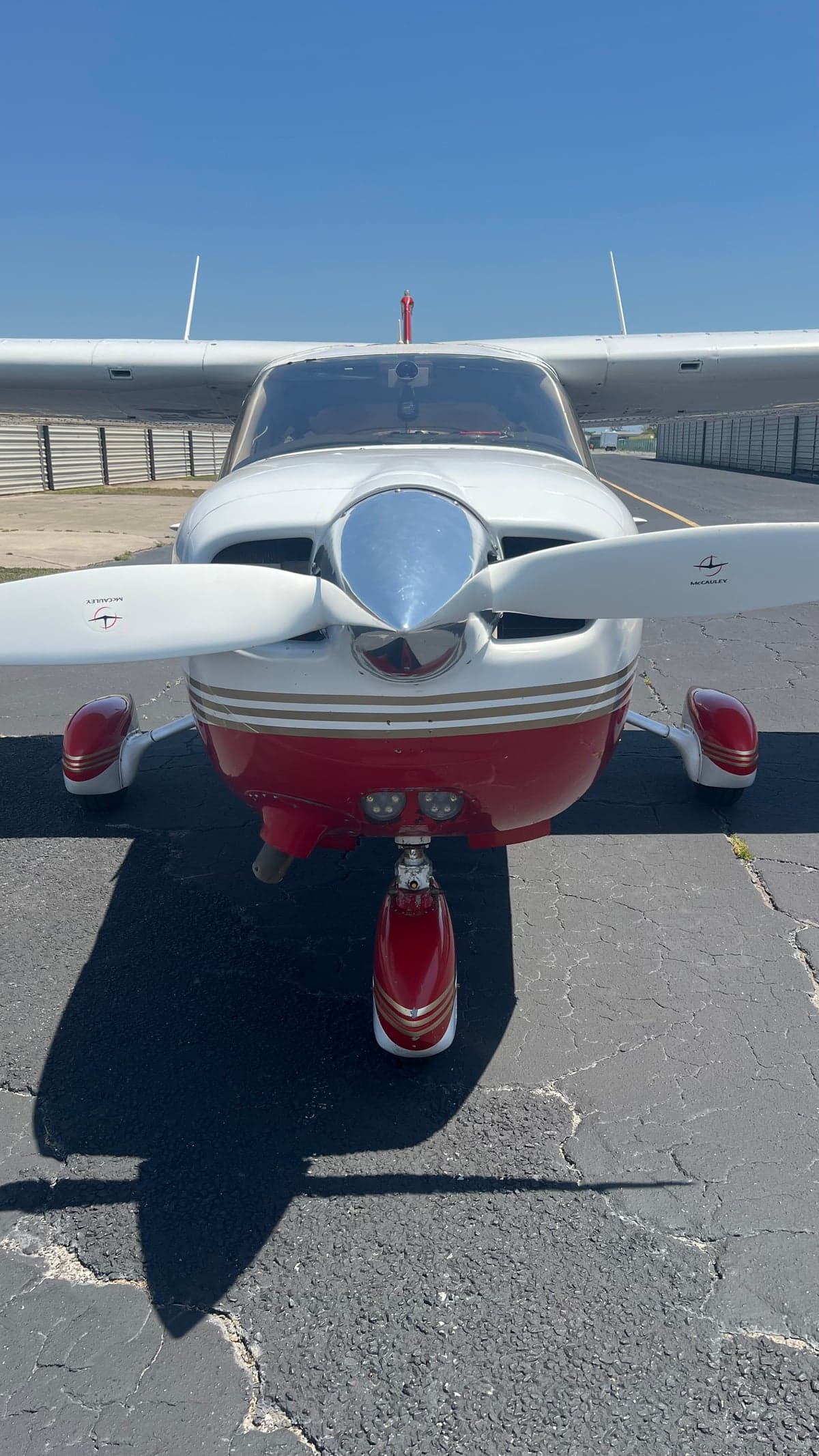 A front view of the white and red aircraft with gold stripes, parked on an asphalt tarmac under a clear blue sky.