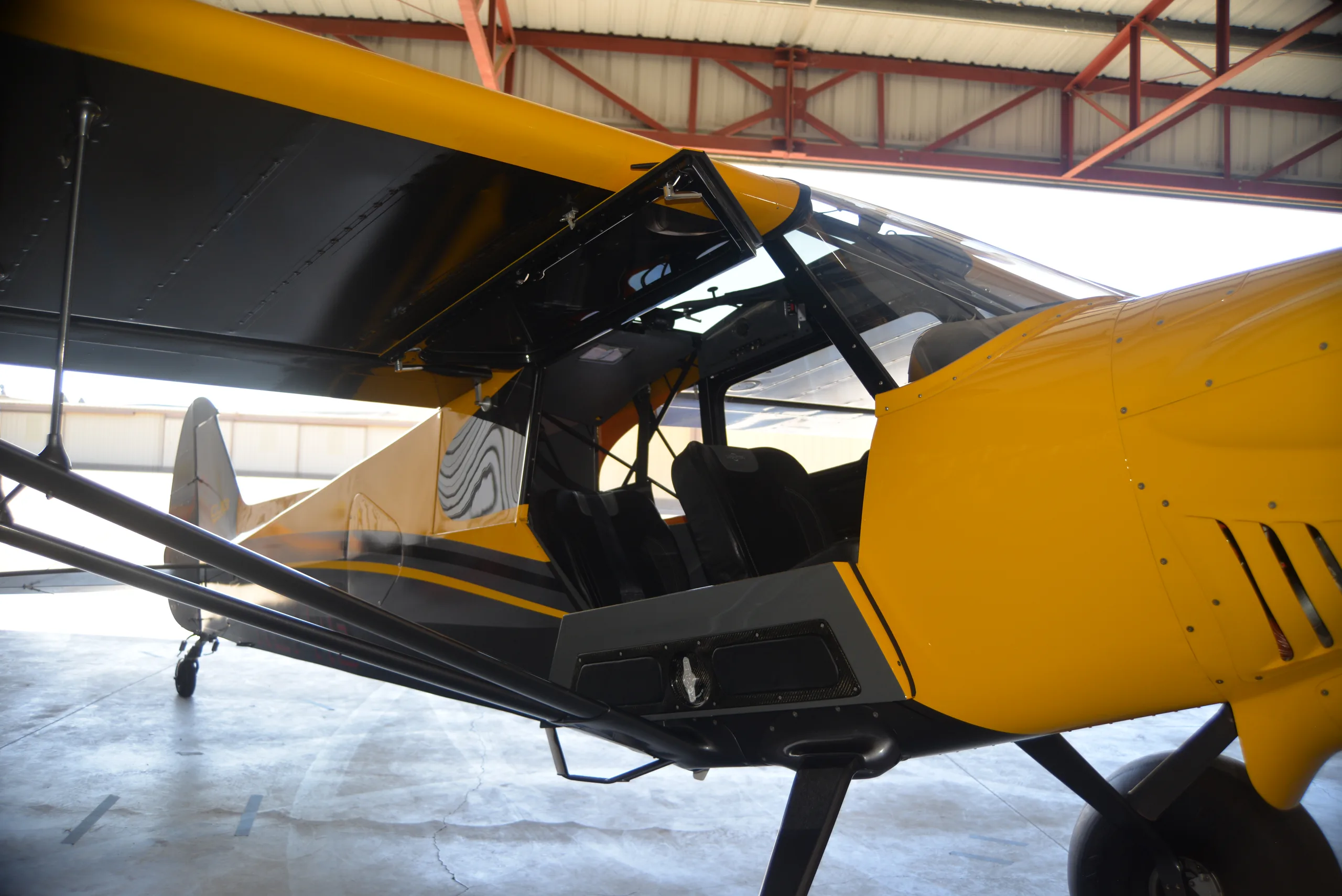 The open door of a yellow and gray CubCrafters XCub, registration N27MB, showing the interior.