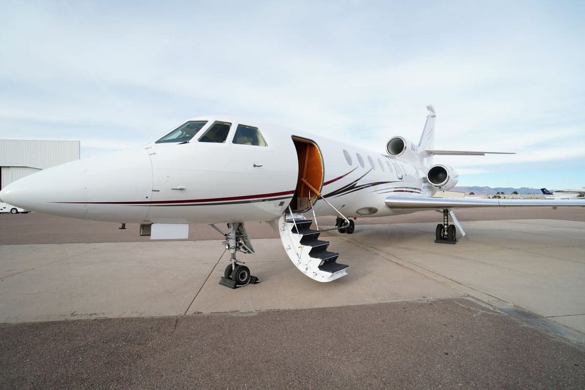 A white Falcon jet with open door and airstair extended.