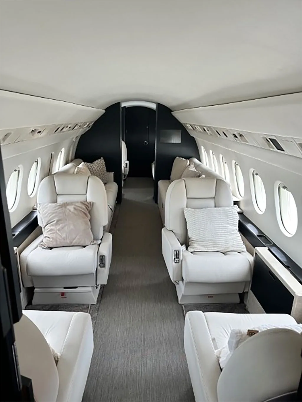 The luxurious cabin interior of the Falcon 900EX, featuring two rows of opposing white leather club seats with throw pillows.