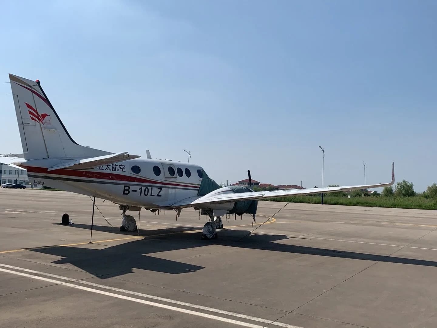 A King Air B-10LZ aircraft is parked on the tarmac with propeller covers, side view.