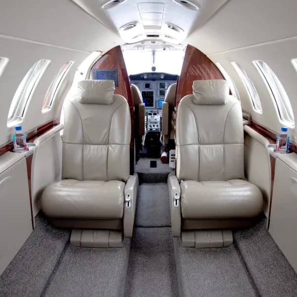 The aircraft cabin interior shows beige leather club seats and a view into the cockpit.