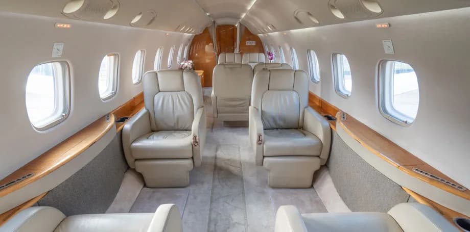 The luxurious interior cabin of a private jet with light beige leather seats and wooden accents.