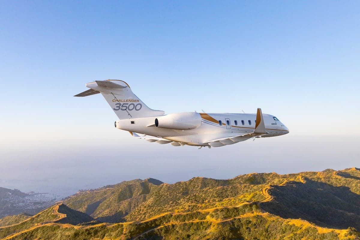A Challenger 3500 aircraft flying over a mountainous landscape.