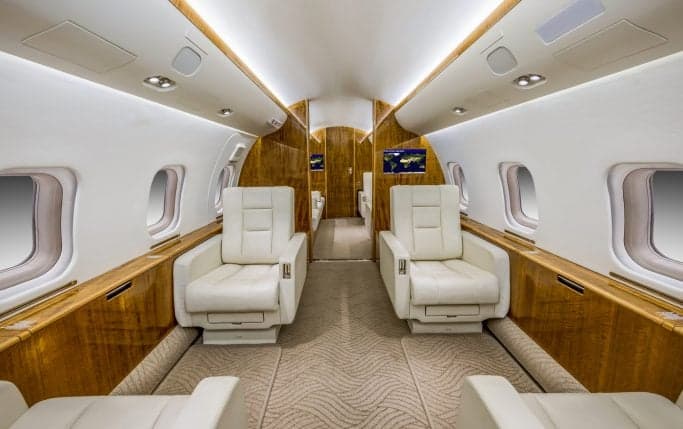 Aircraft interior with white leather seats and wood accents.