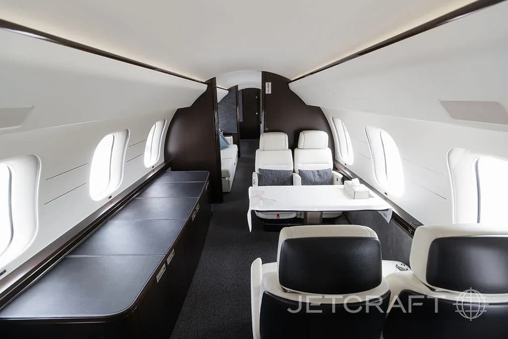 The elegant cabin of a Bombardier Global 7500 featuring white leather seats, a dark table, and a long side credenza.