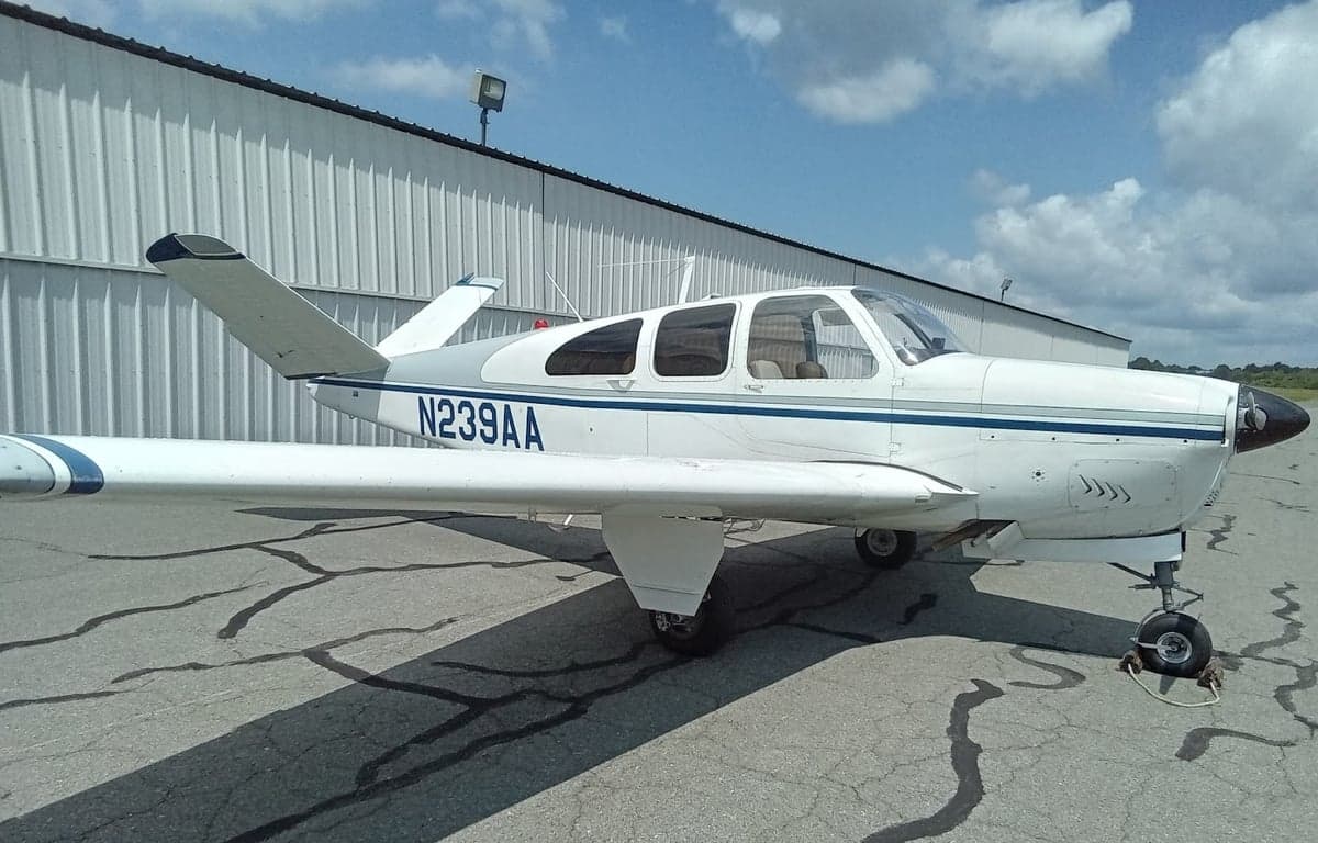 A white and blue Beechcraft Bonanza with registration N239AA parked on the tarmac.