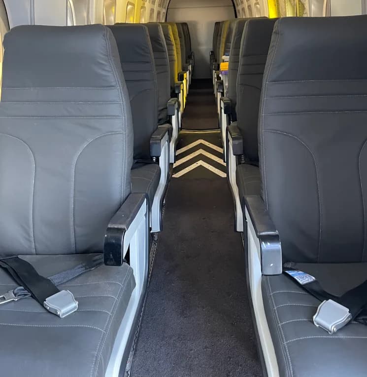 A view down the aisle of an aircraft cabin, showing multiple rows of dark gray passenger seats.