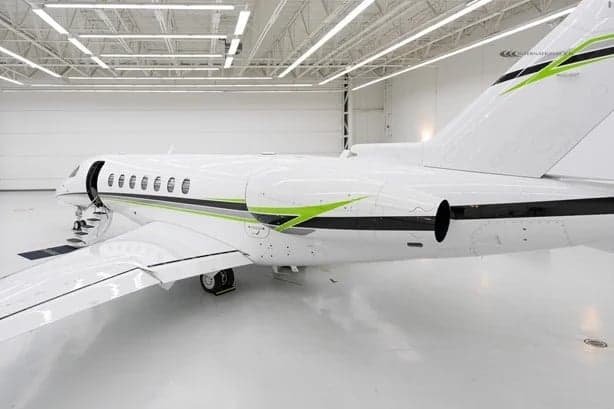 A white jet with green accents is parked in a hangar.