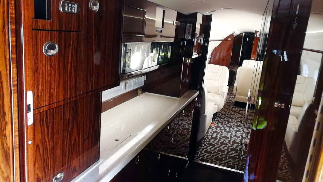 Galley area inside the aircraft cabin with dark wood cabinets and a white countertop, looking towards the seating area.