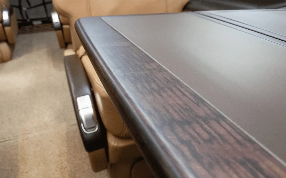A close-up view of a dark wood-grain table surface and a tan leather seat armrest inside the aircraft cabin.