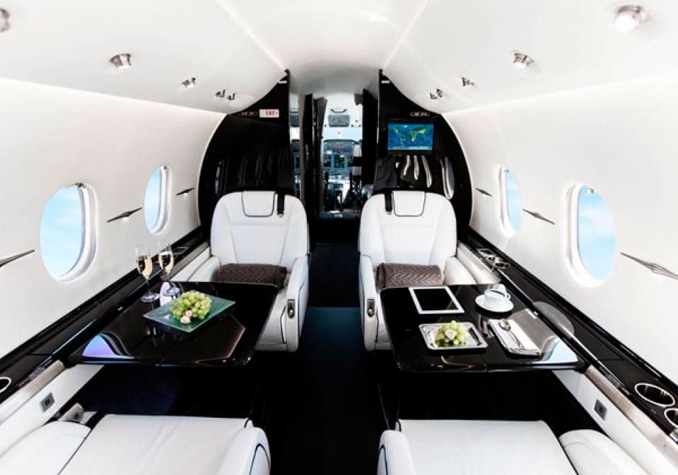 The interior of a Hawker jet with white leather seats and black tables.