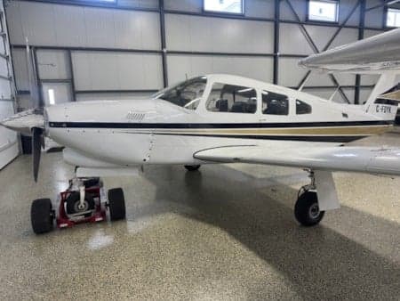 A white low-wing aircraft with black and gold stripes, tail number C-FDYK, parked inside a hangar.