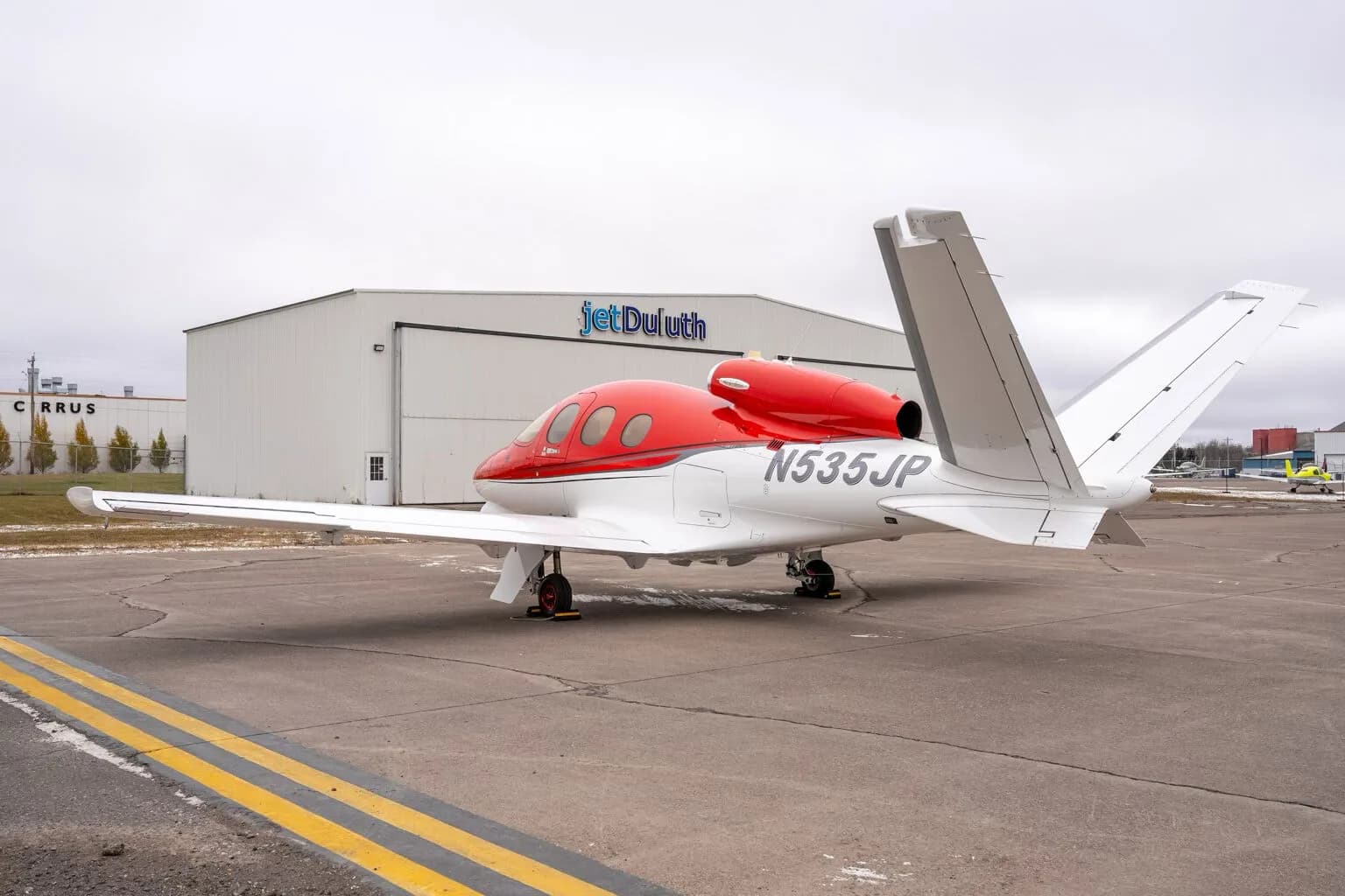 Rear left view of a red and white Cirrus Vision Jet (N535JP) parked in front of a hangar.