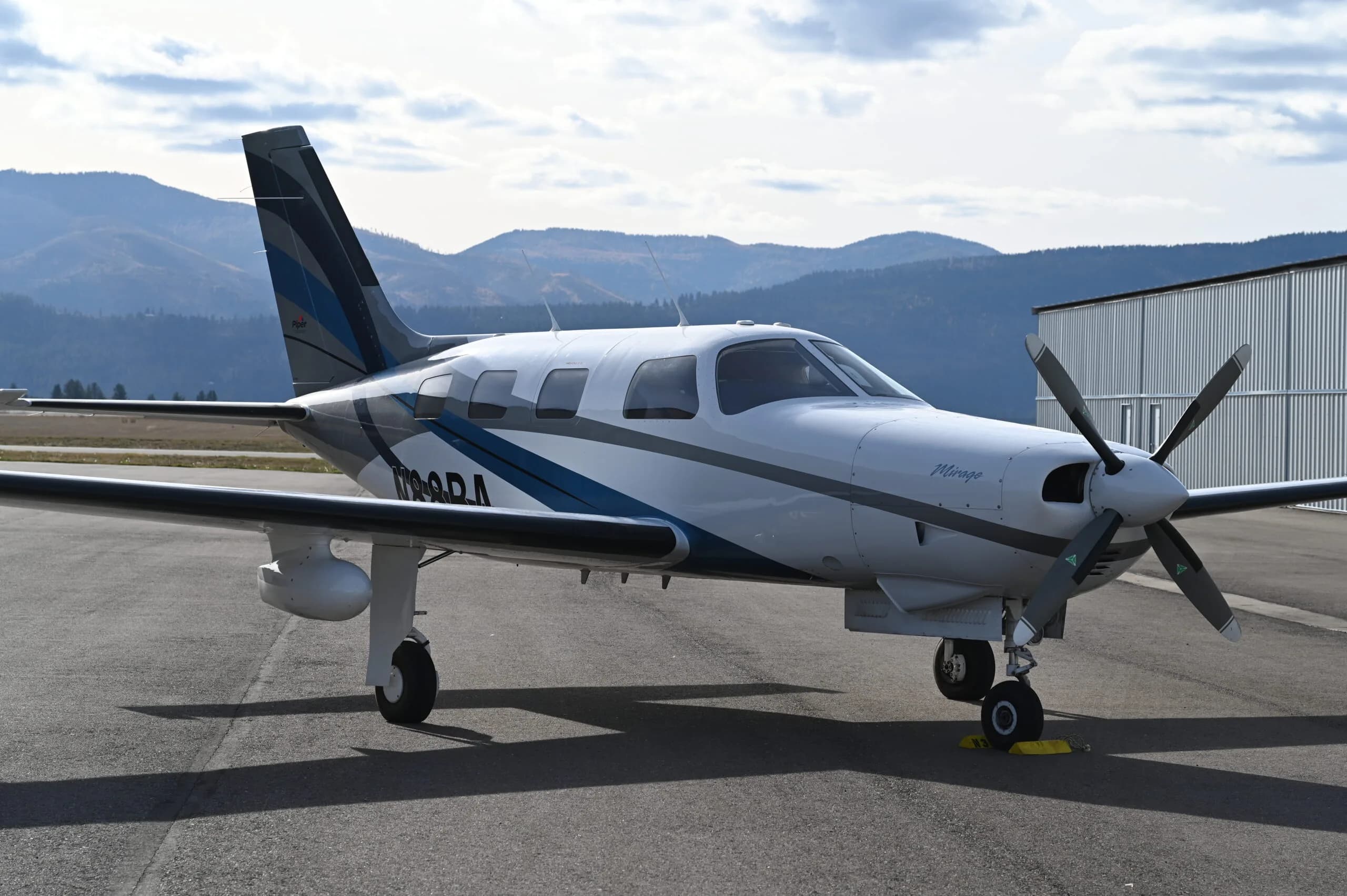 A Piper Mirage aircraft is parked on the tarmac with mountains in the background.