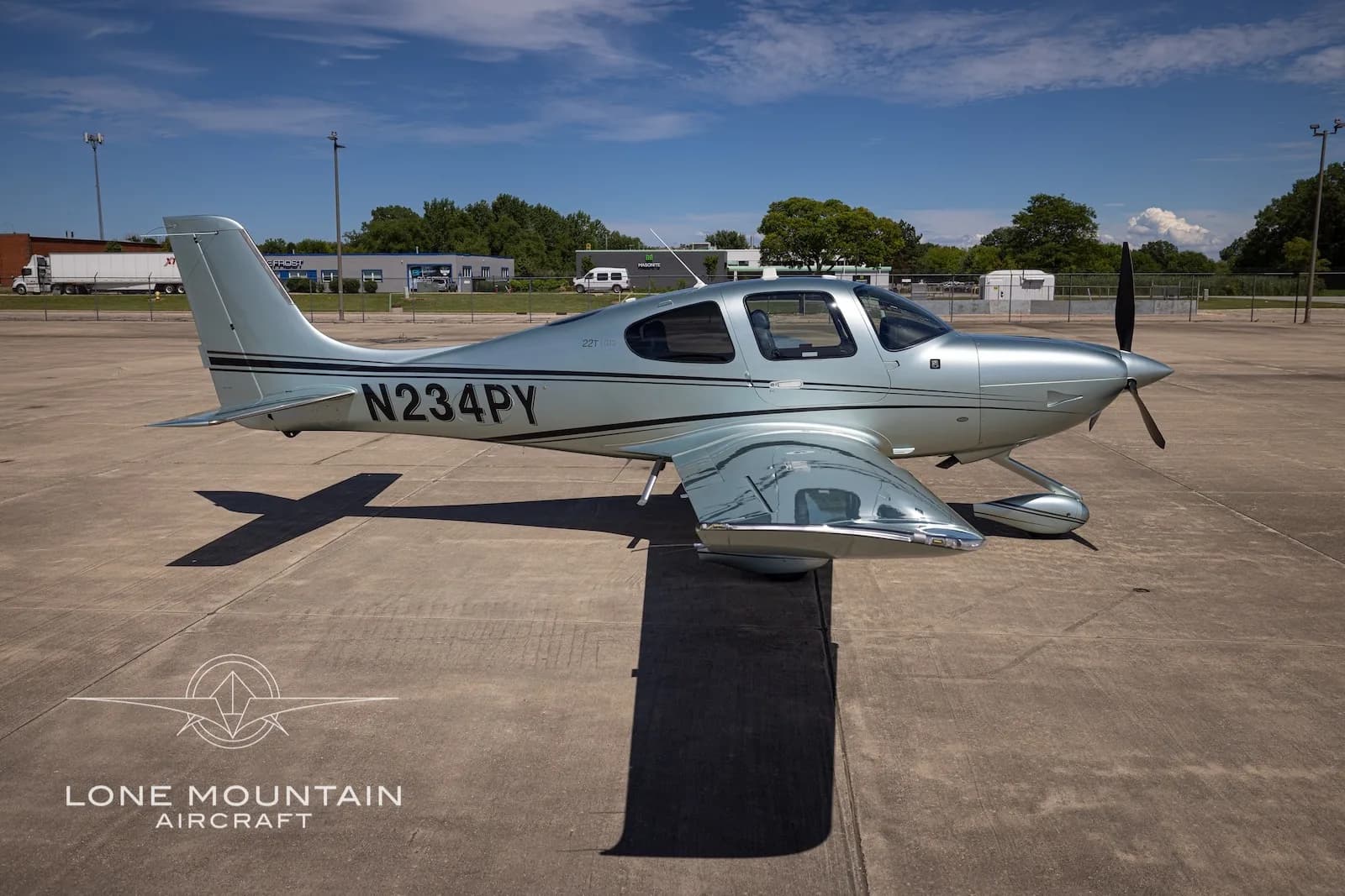 A side view of a silver Cirrus SR22 aircraft (N234PY) with black stripes parked on a tarmac.