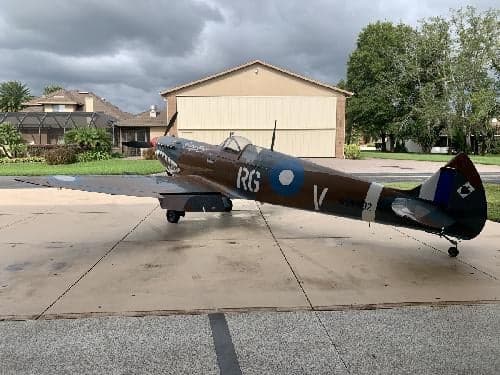 A P-40 Warhawk replica aircraft with shark mouth paint scheme is parked on a concrete pad.