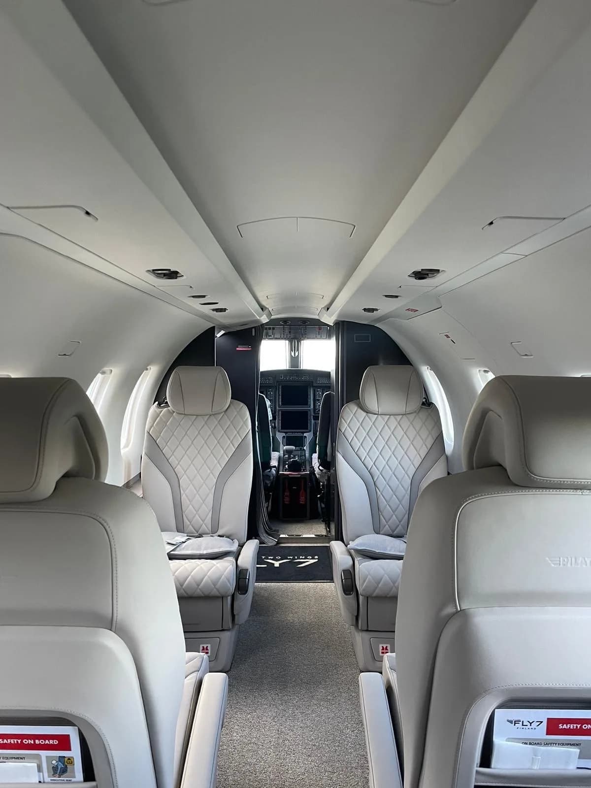 The light gray interior cabin of an aircraft with quilted seats leads to the cockpit visible in the distance.