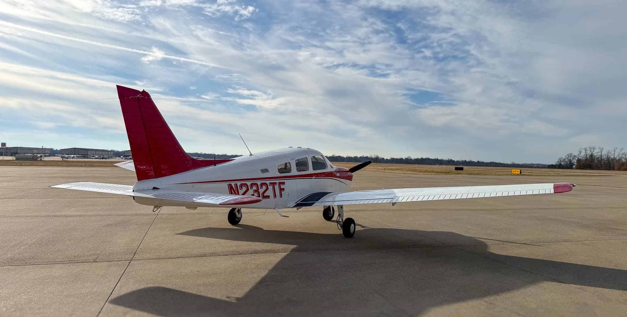 A three-quarter rear-left view of a white and red Piper Archer TX, N232TF, parked on an airfield.