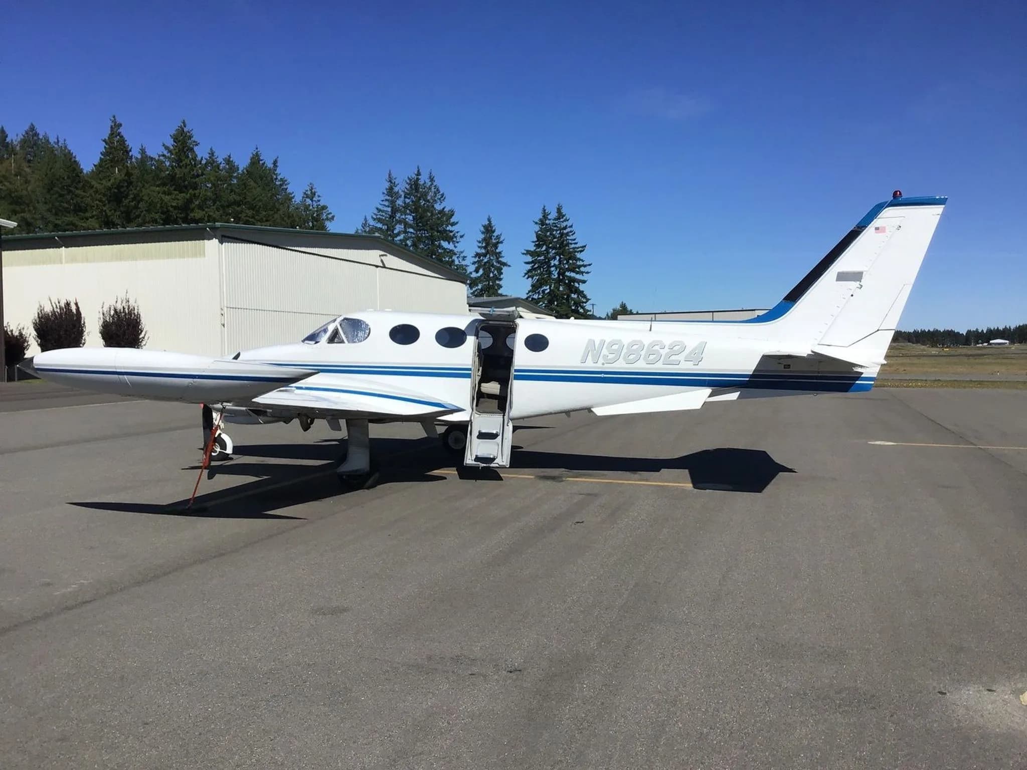 A white and blue twin-engine Cessna 340 aircraft, N98624, with its passenger door open, parked on an airfield.
