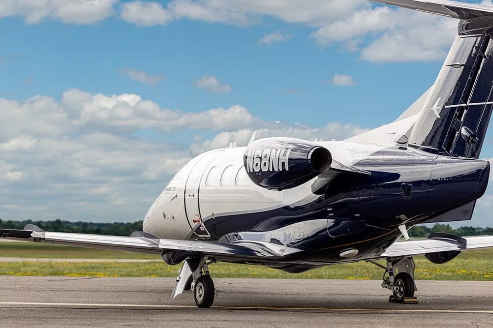 A rear three-quarter view of the white and dark blue Embraer Phenom 100E business jet, N68NH, parked on an airfield.