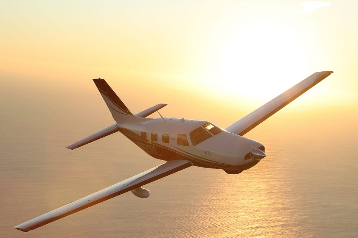 Piper M350 flying over the ocean at sunset.