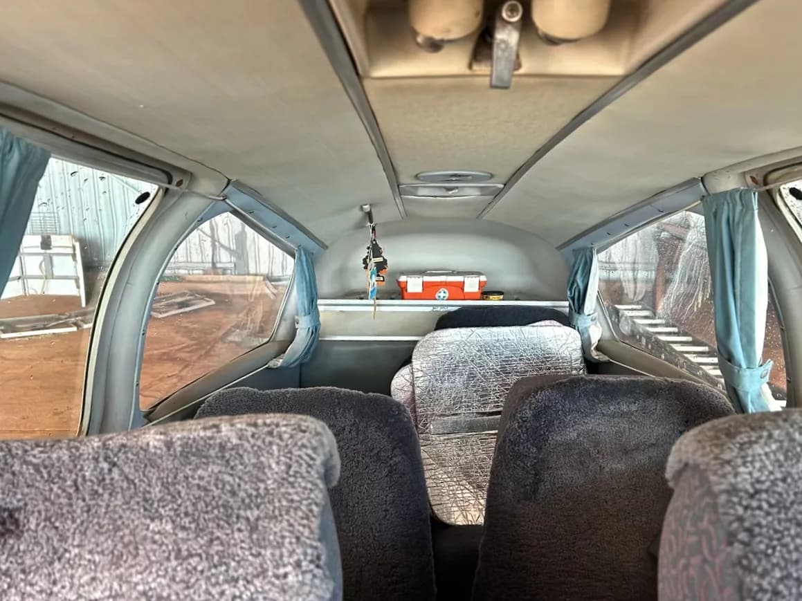 The interior cabin of a small aircraft with grey sheepskin seat covers and a red first aid kit in the rear.