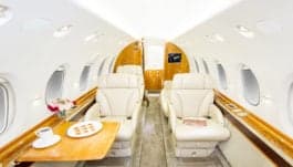 Interior of the aircraft with beige leather seats, wood accents, and a table with a tablet and coffee cup.