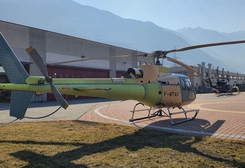 A Eurocopter AS350 Ecureuil helicopter is parked on a helipad in front of a building.