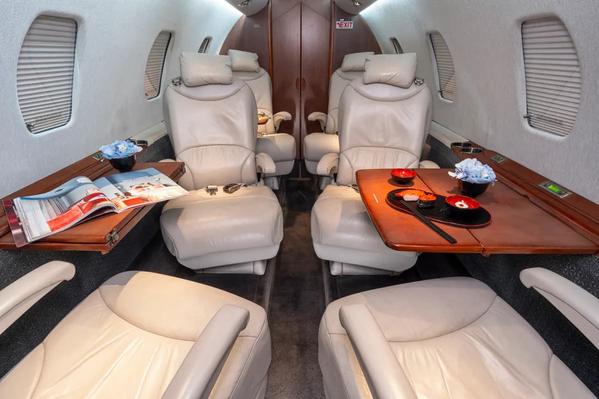 A view of the aircraft's interior, featuring a leather seat and a wooden table with a magazine and a glass of whiskey.