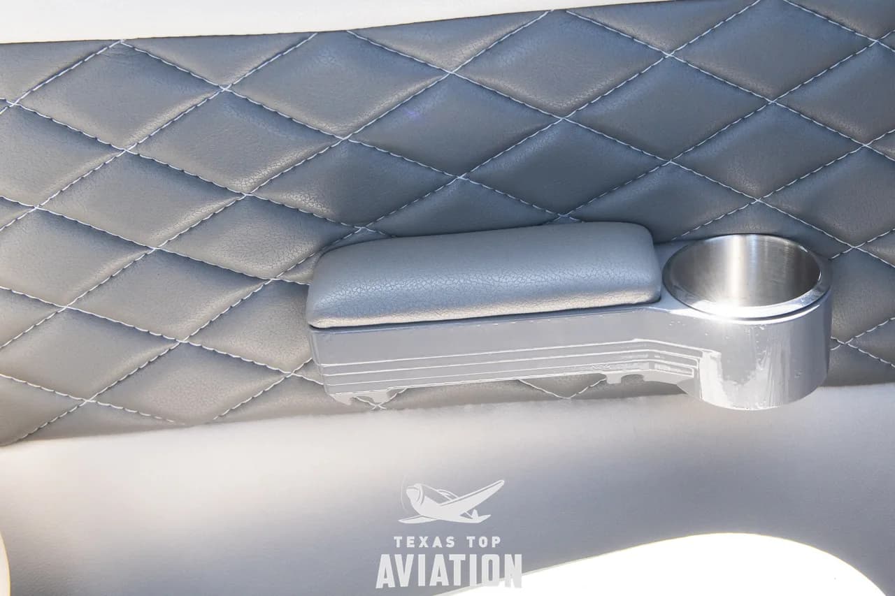 A close-up of a side panel with quilted grey upholstery, an armrest, and a cup holder.