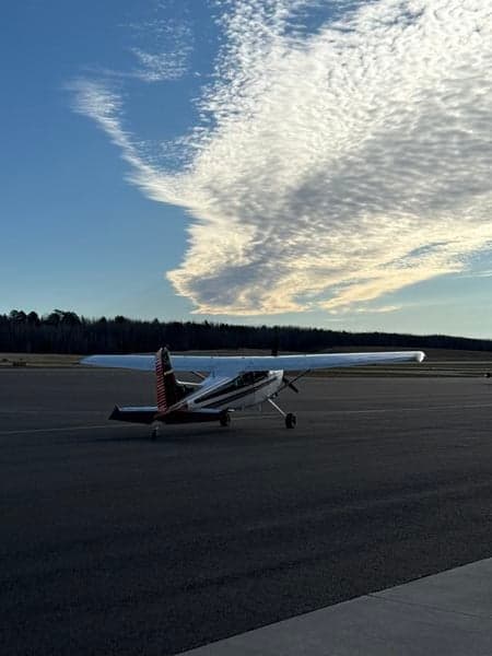 A Cessna 185 Skywagon on the tarmac with a cloudy sky overhead.