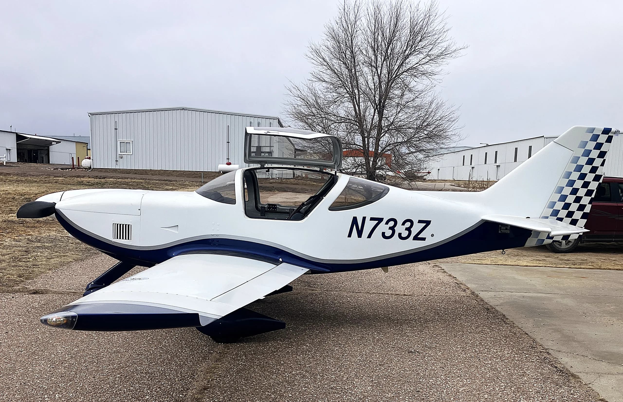 A white and blue Glasair Sportsman aircraft (N733Z) with its canopy open, parked on an airfield, viewed from the right side.
