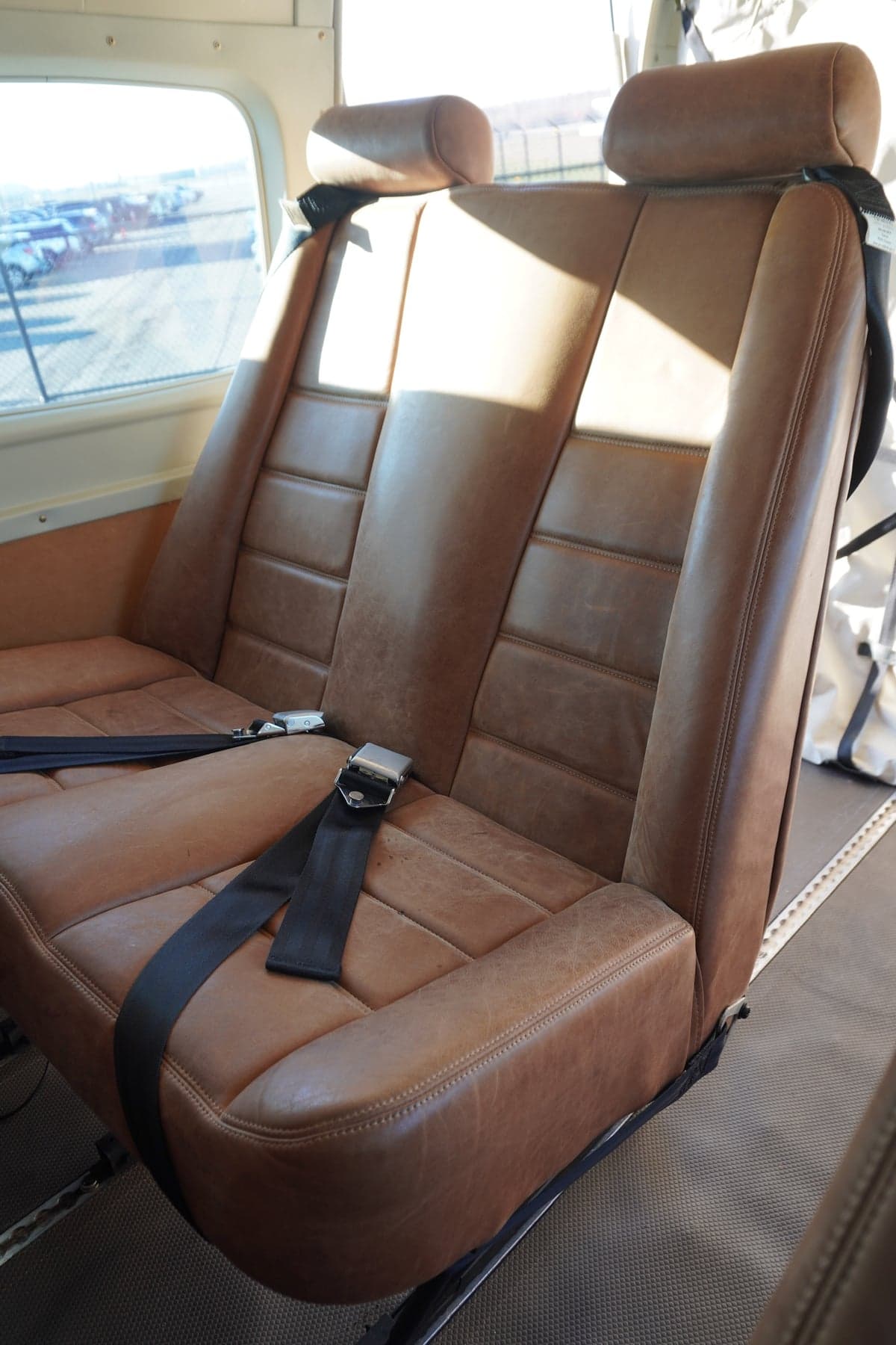 A close-up of two brown leather passenger seats with seatbelts in an aircraft cabin.