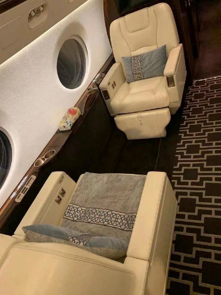 Cream-colored leather seats with blue pillows inside the aircraft cabin, next to a window.