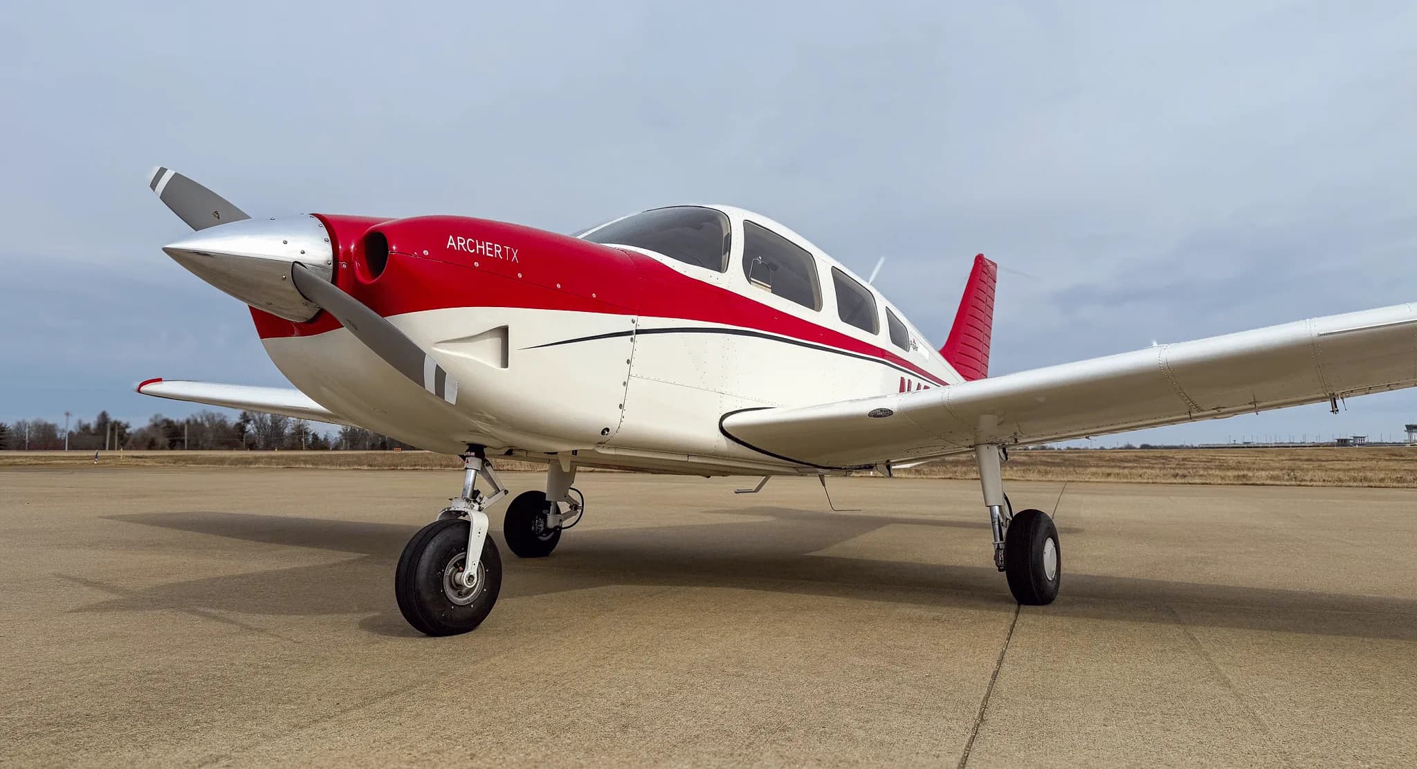 A low-angle front view of a white and red Piper Archer TX aircraft parked on an airfield.