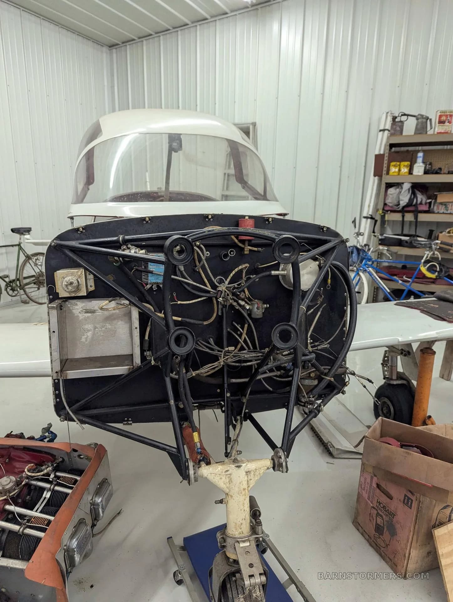 A close-up view of the front of a white aircraft, showing the engine mount, wiring, and nose gear during maintenance.