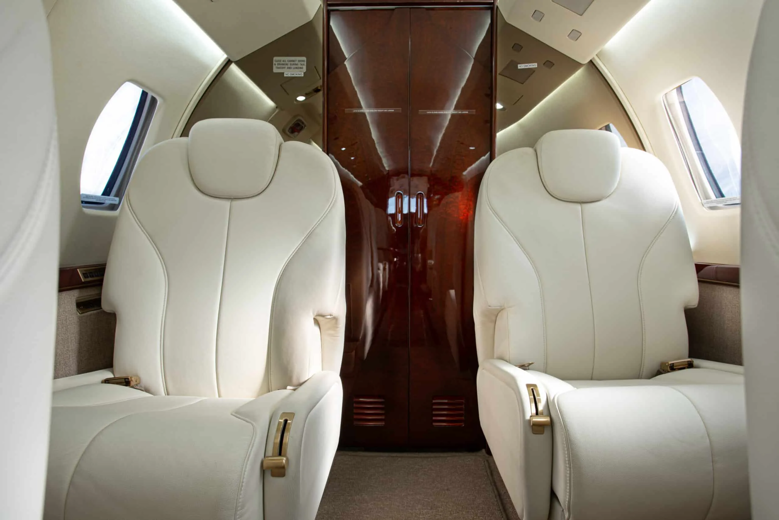 A view of the aircraft cabin showing two cream leather seats and a dark polished wooden door at the rear.