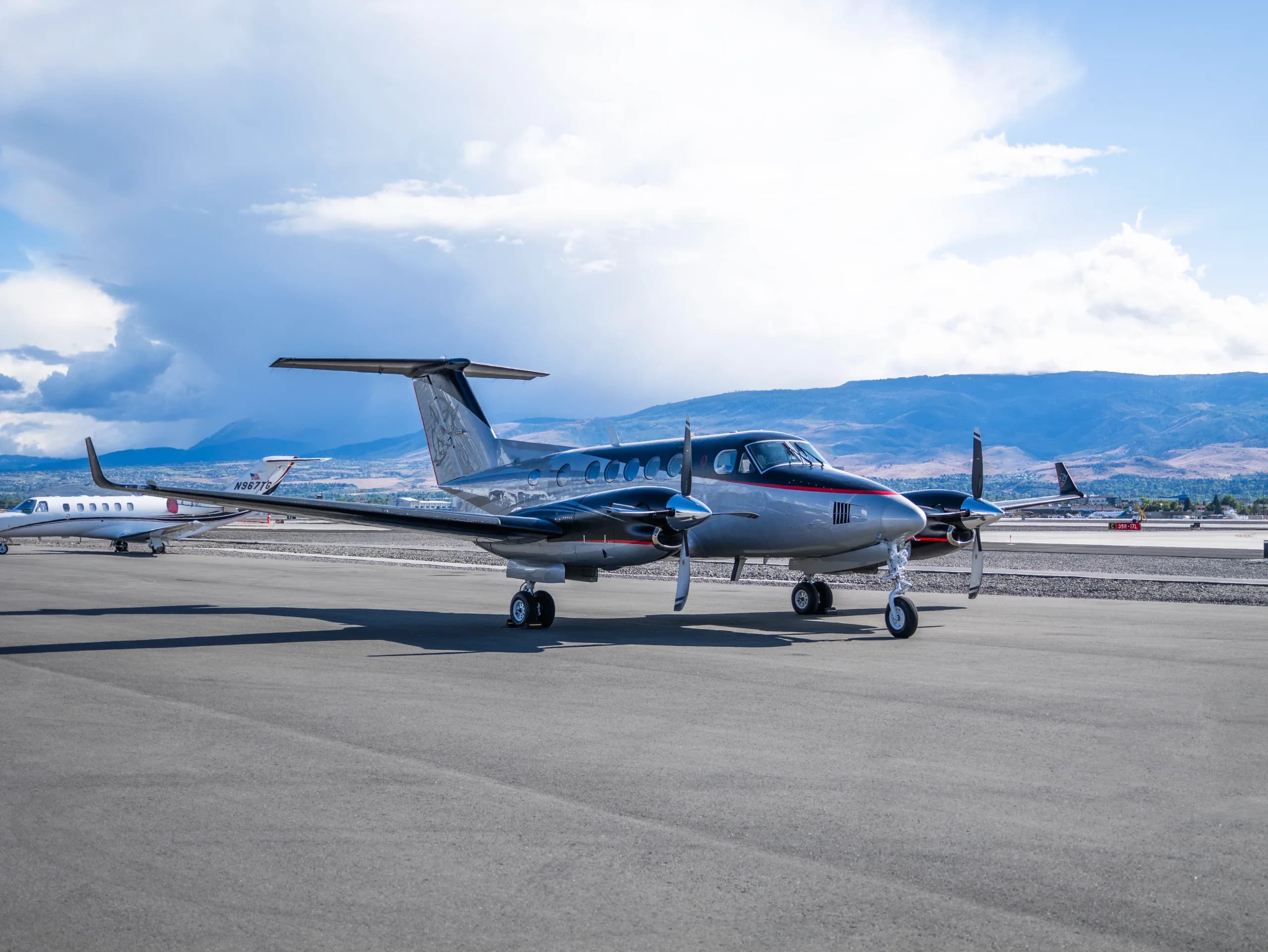 A silver and black twin-turboprop aircraft with red accents and a custom tail logo parked on an airport tarmac.