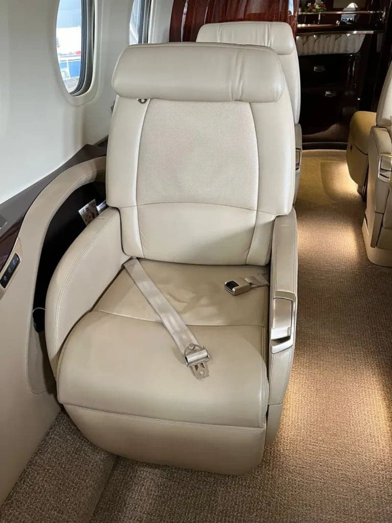 A single tan leather seat with a seatbelt in the aircraft cabin.