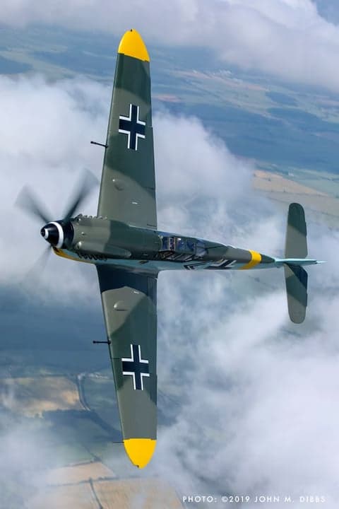 Close-up of a Messerschmitt Bf 109 aircraft in flight, with clouds in the background.