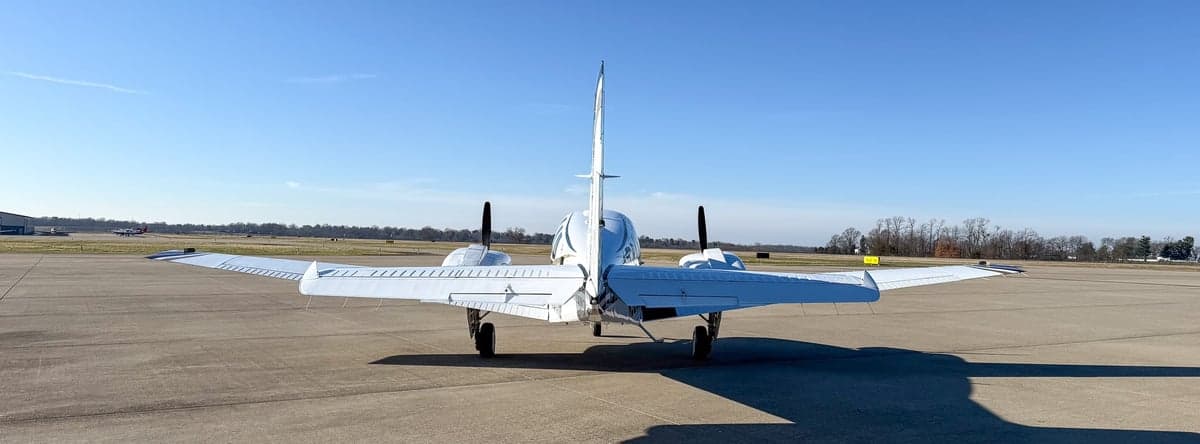 Rear view of a white twin-engine propeller aircraft on an airfield.
