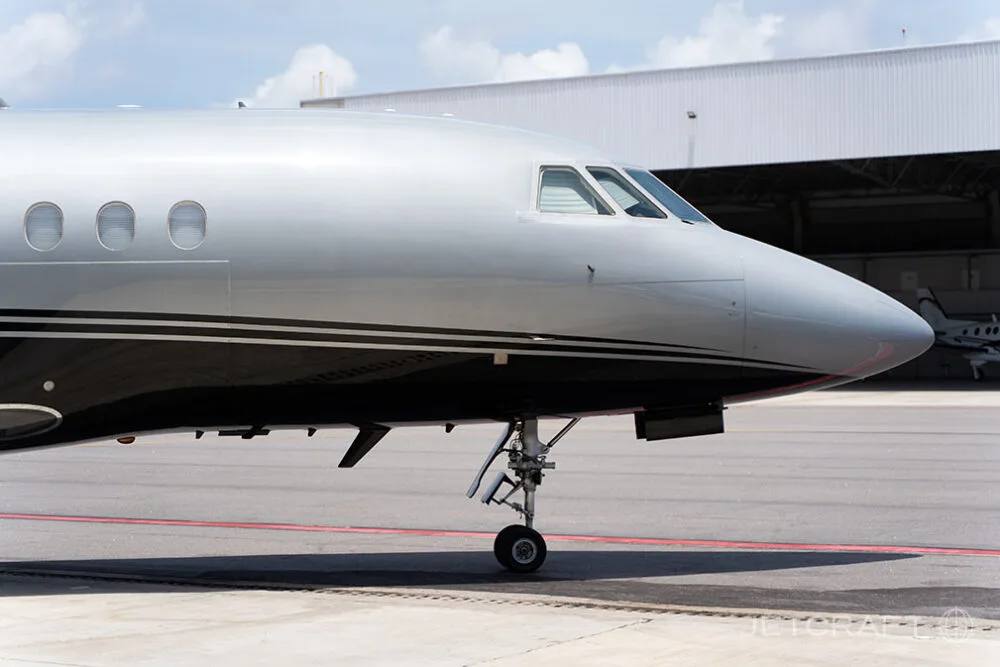 A close-up side view of the nose and cockpit windows of a silver and black business jet.
