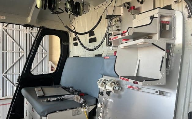 The helicopter's interior features a blue bench seat and storage compartments.