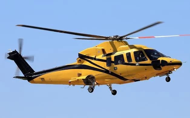 A yellow and black helicopter with its rotors spinning is captured in flight against a clear blue sky.